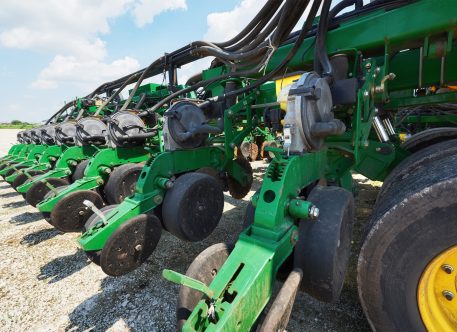 Como a conectividade pode aumentar a eficiência das suas máquinas? Close up of seeder attached to tractor in field. Agricultural machinery for spring works sowing, seeding