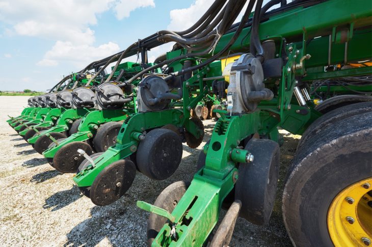 Como a conectividade pode aumentar a eficiência das suas máquinas? Close up of seeder attached to tractor in field. Agricultural machinery for spring works sowing, seeding